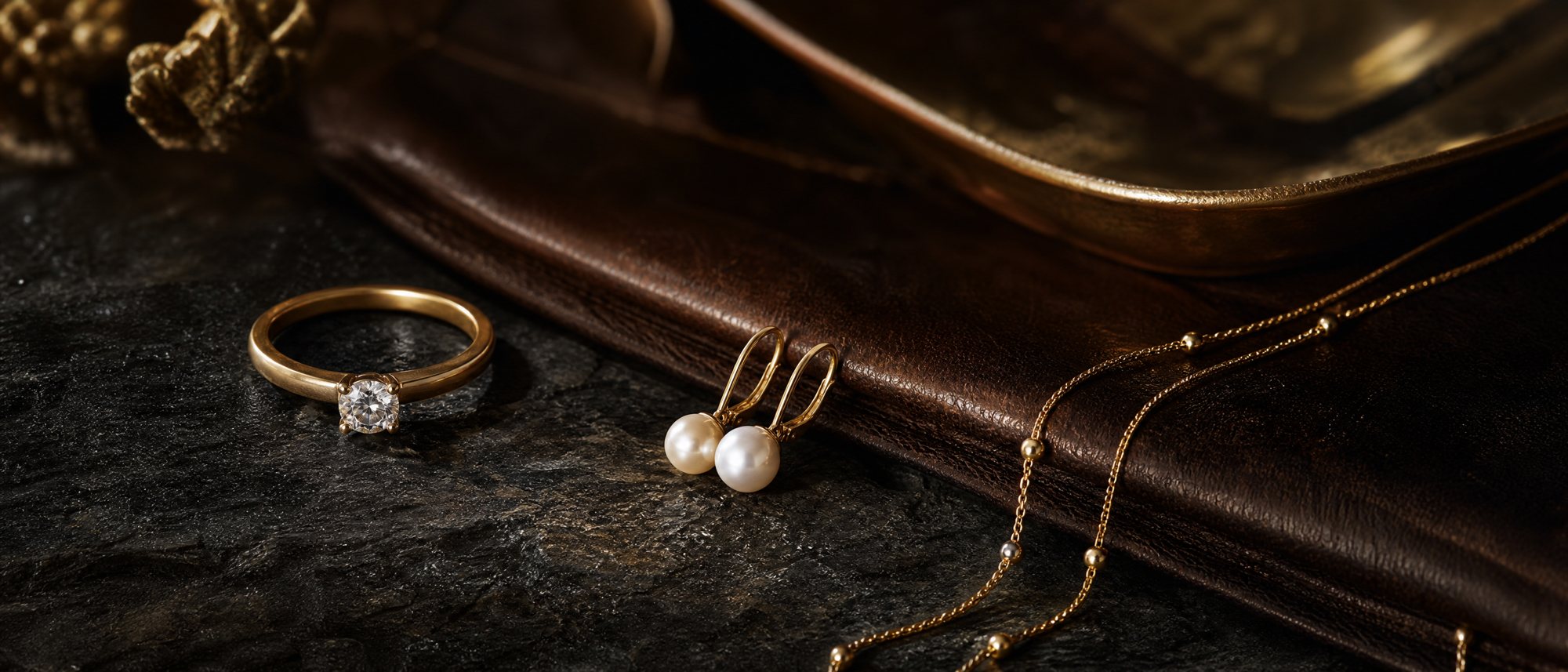 Selección de joyería sobre piedra oscura y piel: solitario, pendientes de perla y cadenas de oro